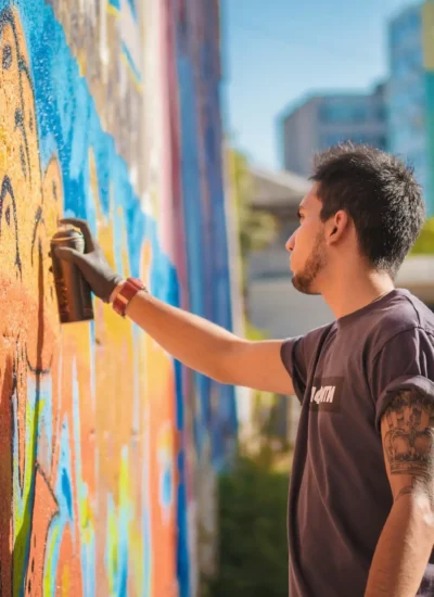 Handsome Talented Young Boy making a colorful graffiti with aerosol spray on urban street wall