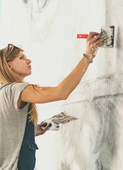 Young beautiful girl painting big graffiti of woman’s face. Street Art Concept.